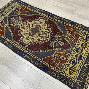 May include: A rectangular area rug featuring a central medallion in shades of cream, blue, and rust red set against a dark charcoal field. The border displays intricate geometric patterns in yellow, blue, and rust, finished with short white fringe.