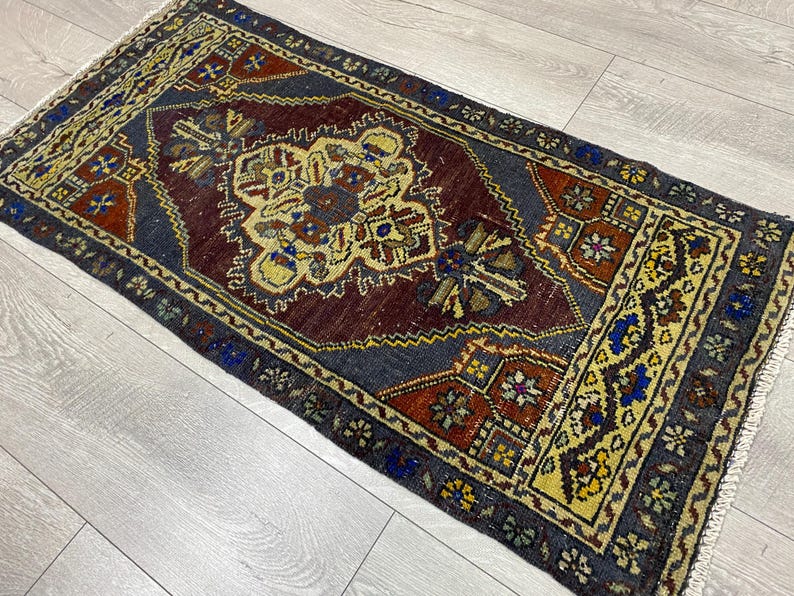 May include: A rectangular area rug featuring a central medallion in shades of cream, blue, and rust red set against a dark charcoal field. The border displays intricate geometric patterns in yellow, blue, and rust, finished with short white fringe.