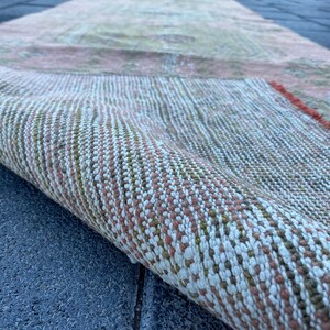May include: Close-up of a woven rug with a pink, white, and green pattern. The rug is rolled up and the edge of the rug is visible.