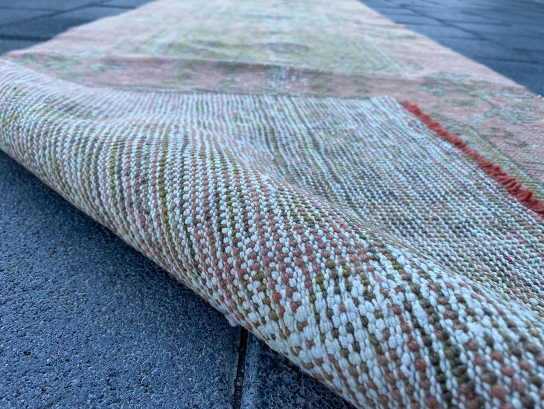 May include: Close-up of a woven rug with a pink, white, and green pattern. The rug is rolled up and the edge of the rug is visible.