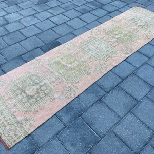 May include: A pink and cream runner rug with a floral pattern. The rug has a distressed look and is made of a soft, woven material.