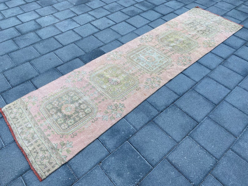 May include: A pink and cream runner rug with a floral pattern. The rug has a distressed look and is made of a soft, woven material.