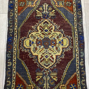 May include: A rectangular woven rug featuring a central diamond medallion in cream, surrounded by a deep burgundy field. The design includes intricate geometric and floral motifs in shades of blue, yellow, and rust, framed by a dark blue border.