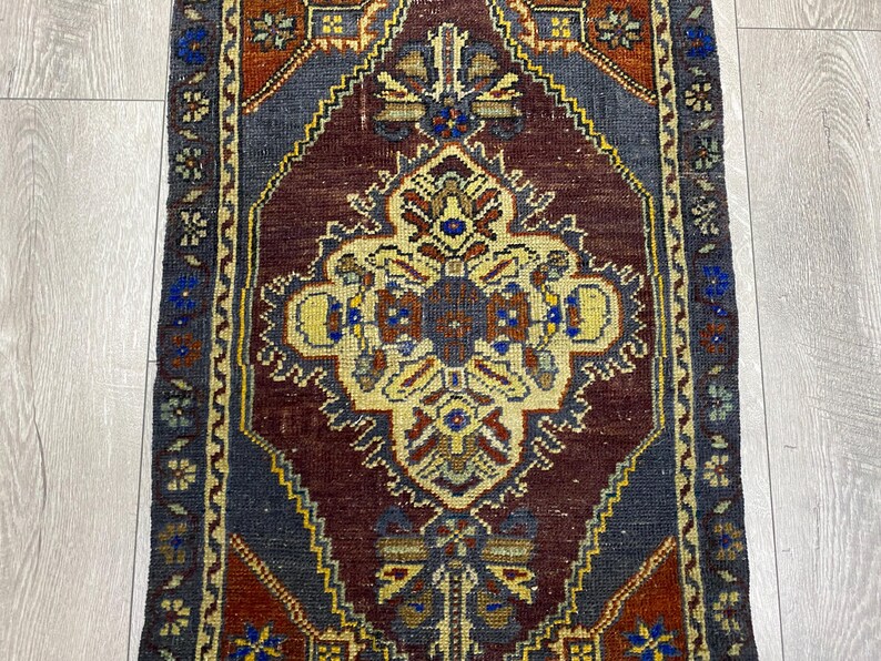May include: A rectangular woven rug featuring a central diamond medallion in cream, surrounded by a deep burgundy field. The design includes intricate geometric and floral motifs in shades of blue, yellow, and rust, framed by a dark blue border.