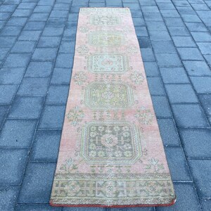 May include: A pink and green vintage runner rug with a geometric pattern. The rug has a faded look and is made of wool.