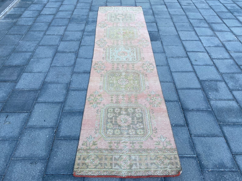 May include: A pink and green vintage runner rug with a geometric pattern. The rug has a faded look and is made of wool.