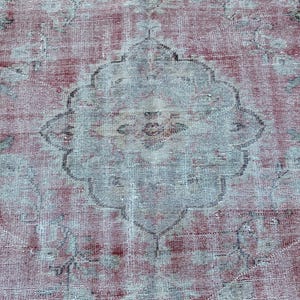 May include: A vintage rug with a faded red and white color scheme. The rug has a central medallion design with intricate floral patterns. The rug is worn and distressed, giving it a rustic and antique look.