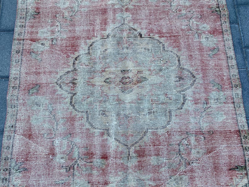 May include: A vintage rug with a faded red and white color scheme. The rug has a central medallion design with intricate floral patterns. The rug is worn and distressed, giving it a rustic and antique look.