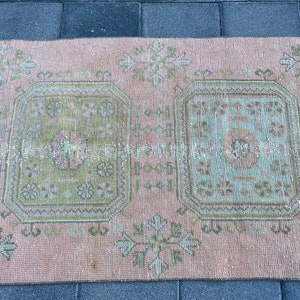 May include: A vintage pink and green rug with a geometric pattern. The rug has two large squares in the center with a smaller pattern inside. The rug is faded and worn, giving it a distressed look.