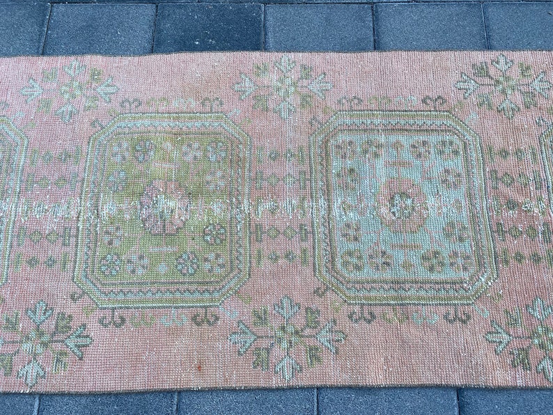 May include: A vintage pink and green rug with a geometric pattern. The rug has two large squares in the center with a smaller pattern inside. The rug is faded and worn, giving it a distressed look.