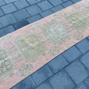 May include: A pink and green vintage runner rug with a geometric pattern. The rug has a faded look and is made of a soft, woven material.