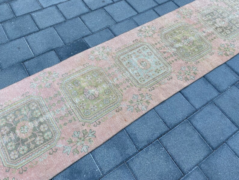 May include: A pink and green vintage runner rug with a geometric pattern. The rug has a faded look and is made of a soft, woven material.