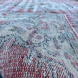 May include: Close-up of a red and cream colored woven rug with a geometric pattern. The rug is made of a soft, textured material.