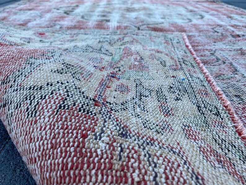 May include: Close-up of a red and cream colored woven rug with a geometric pattern. The rug is made of a soft, textured material.
