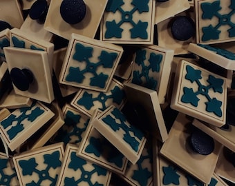 Peut inclure: Gros plan sur un tas de carreaux en céramique beige avec un motif géométrique bleu sarcelle. Les carreaux ont un bord légèrement surélevé et une surface lisse.