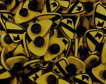 Peut inclure: Gros plan sur une collection de patchs en tissu jaune et noir avec un motif stylisé d'une étoile et d'un numéro. Les patchs sont disposés de manière aléatoire et sont de tailles différentes.