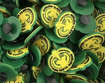 Peut inclure: Gros plan sur de nombreux breloques de chaussures vertes et jaunes. Chaque breloque présente un motif circulaire avec un emblème jaune et le texte "WE'LL BE THERE". Les breloques ont un bouton noir à l'arrière pour la fixation.
