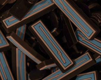 Peut inclure: Gros plan sur un tas de patchs rectangulaires noirs et bleus avec un contour blanc et un petit motif blanc représentant un fusil à l'intérieur. Les patchs sont faits d'un matériau souple et flexible.