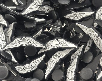 Peut inclure: Un ensemble de breloques de chaussures noires et blanches avec un motif d'emblème ailé. Les breloques ont une base noire avec une aile blanche détaillée et un motif de bouclier, créant un contraste. Ces breloques sont pour personnaliser les chaussures.