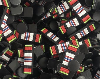 Peut inclure: Un tas de breloques en forme de ruban rayé noir et rouge avec un cercle noir au centre. Les breloques sont en silicone et ont une finition brillante.