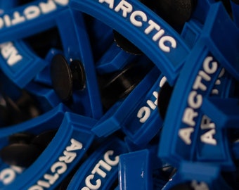 Peut inclure: Gros plan sur un tas de colliers de serrage en plastique bleu avec le mot "ARCTIC" imprimé en blanc sur chaque collier.