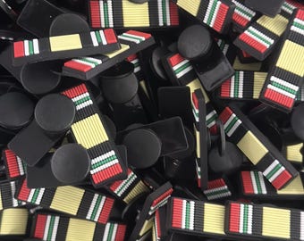 Peut inclure: Gros plan sur un tas de breloques en ruban noir et blanc avec des accents rouges et verts. Les breloques sont en forme de ruban et ont un schéma de couleurs jaune, blanc, rouge et vert. Les breloques sont disposées de manière aléatoire et sont toutes orientées dans la même direction.