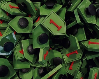 Peut inclure: Gros plan sur un tas de pièces de jeu en plastique vert avec le numéro "1" imprimé dessus. Chaque pièce a un bouton noir au dos.