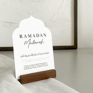 Könnte beinhalten: Eine weiße Karte mit einem Bogen oben. Die Karte sagt "Ramadan Mubarak" in schwarzer Kalligraphie. Die Karte enthält auch arabischen Text und eine Botschaft in Deutsch, die lautet: "O Allah, ich habe um Deinetwillen gefastet. Ich glaube an Dich, ich vertraue auf Dich und ich breche mein Fasten mit deiner Versorgung."