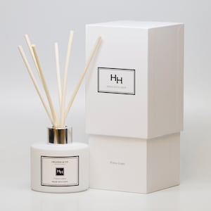 May include: White cylindrical glass bottle with a silver lid and wooden sticks, filled with a clear liquid. The bottle has a label that reads "Helena & Co. Perfumes" and "Fresh Linen Reed Diffuser". The bottle is sitting on a white surface next to a white box with the text "HH Reed Diffuser" and "Fresh Linen" printed on it.