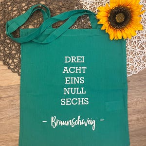 Könnte beinhalten: Eine grüne Stofftasche mit weißem Text, der "Drei Acht Eins Null Sechs - Braunschweig - " lautet.