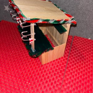 May include: A small wooden Christmas market stall with a green roof and red and white candy cane trim. The stall has hooks on the side for hanging items.