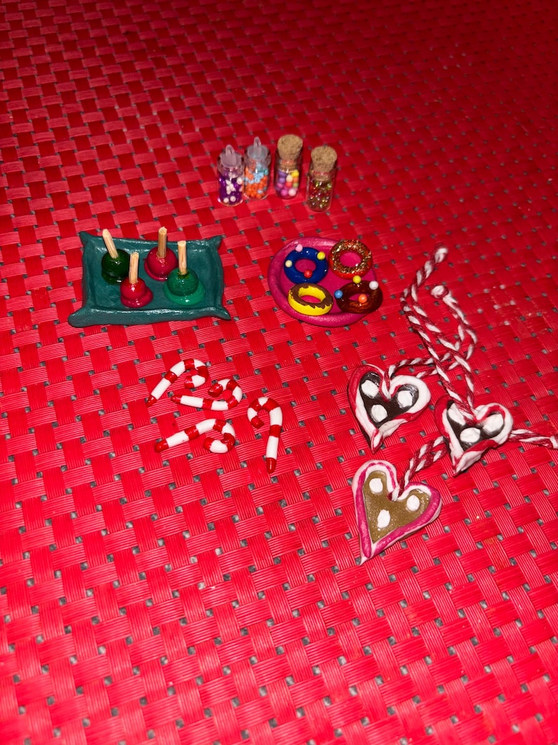 May include: A collection of miniature candy and sweets made from polymer clay. The set includes candy canes, heart-shaped cookies, donuts, and candy apples. There are also three small jars filled with colorful sprinkles.