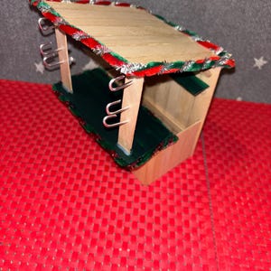 May include: A small wooden Christmas market stall with a green and red candy cane trim. The stall has hooks on the sides and a green floor.