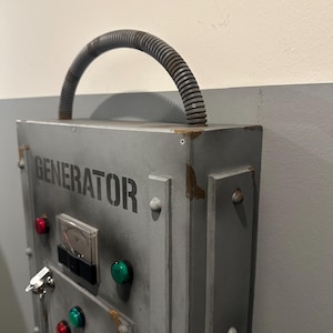 May include: A gray metal box with the word "GENERATOR" printed on the front. The box has a handle made of a flexible gray hose. There are several red and green buttons on the front of the box.
