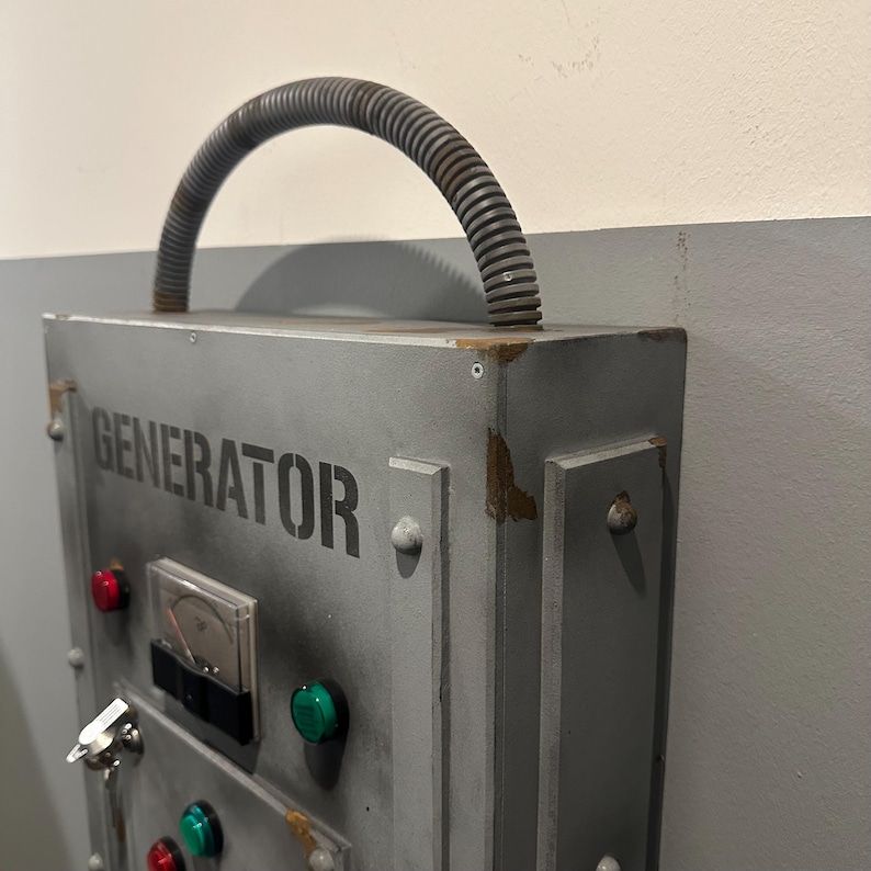 May include: A gray metal box with the word "GENERATOR" printed on the front. The box has a handle made of a flexible gray hose. There are several red and green buttons on the front of the box.