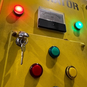 May include: A yellow metal panel with a keyhole, a gauge, and several round buttons. The buttons are red, green, blue, and yellow. The panel has the word "ATOR" printed on it.