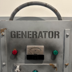 May include: A gray metal panel with the word "GENERATOR" printed in black. The panel has a red button, a green button, and a round gauge with a needle pointing to the right. A gray corrugated hose is attached to the top of the panel.