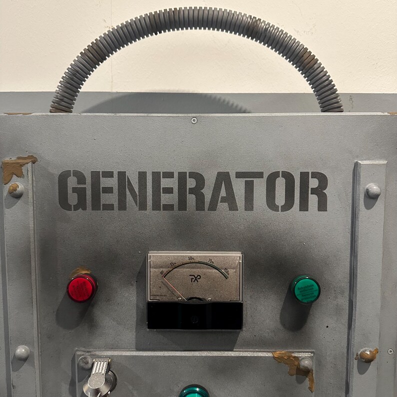 May include: A gray metal panel with the word "GENERATOR" printed in black. The panel has a red button, a green button, and a round gauge with a needle pointing to the right. A gray corrugated hose is attached to the top of the panel.
