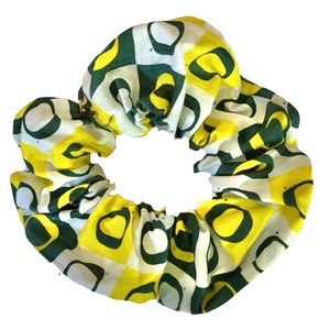 May include: A green and yellow scrunchie with a checkered pattern. The scrunchie is made of fabric and has a white background with green and yellow squares. The squares have a green outline and a yellow interior.