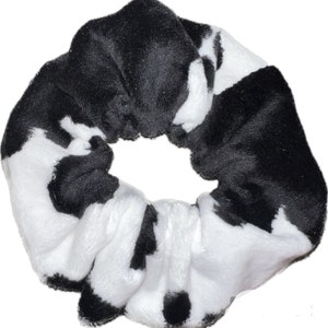 May include: Black and white cow print scrunchie hair tie. The scrunchie is made of soft, fuzzy fabric.