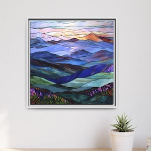 May include: Framed artwork depicting a mountain landscape in shades of blue, purple, and green. The artwork features a stylized, stained-glass effect with a sunset in the background. The frame is white, and the artwork is displayed on a white wall.