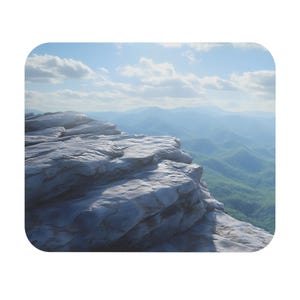 May include: A mousepad featuring a scenic mountain landscape. The image shows a rocky cliff in the foreground with a view of rolling green hills and mountains in the distance under a blue sky with clouds. The mousepad has rounded corners.
