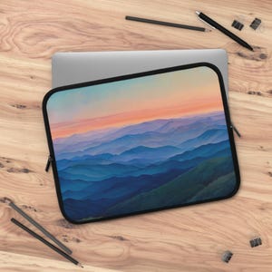 May include: A laptop sleeve with a colorful sunset over a mountain range. The mountains are blue and purple, and the sky is a gradient of pink, orange, and yellow.