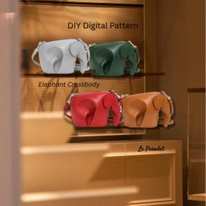 Peut inclure: Plusieurs sacs à bandoulière en forme d'éléphant, de couleurs grise, verte, rouge et beige. Chaque sac est doté d'une bandoulière et d'un détail de trompe. Le texte "DIY Digital Pattern" et "Elephant Crossbody" sont visibles.