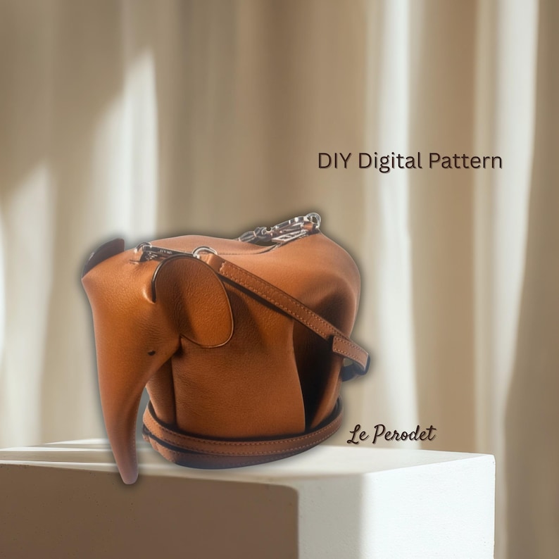 K&ouml;nnte beinhalten: Braune, lederne, elefantenf&ouml;rmige Handtasche mit Schulterriemen und silbernem Kettenhenkel. Die Tasche hat einen R&uuml;ssel und Ohren, mit dem Text "DIY Digital Pattern" und "Le Perodet".