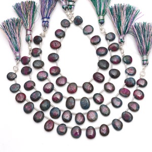 May include: Four strands of oval-shaped ruby and kyanite gemstone beads arranged in a cascading pattern. Each strand is finished with a decorative tassel featuring green, white, and purple threads bound by a silver-colored metal cap and jump ring.
