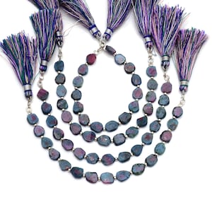 May include: Four strands of dark blue and purple gemstone beads with silver spacers. The beads are faceted and have a rough, natural look. Each strand is finished with a colorful tassel.