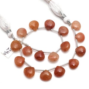 May include: A strand of heart-shaped sunstone beads in shades of peach and orange, strung with silver-toned metal spacers and finished with white tassels at each end. A small white tag with the handwritten number 240 is attached to the strand.