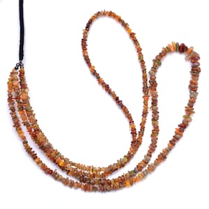 Könnte beinhalten: Eine mehrreihige Halskette aus kleinen, unregelmäßigen, braunen und orangefarbenen Opalperlen. Die Halskette besteht aus drei Perlenreihen und hat einen schwarzen Kordelverschluss.