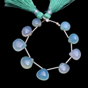 Puede incluir: Un collar de cuentas de piedras preciosas azul claro con forma de lágrima. Las cuentas están ensartadas en un alambre plateado y están acentuadas con una borla turquesa. Las cuentas tienen aproximadamente 1 cm de diámetro.